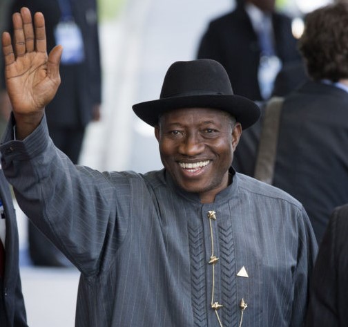 Goodluck Jonathan, former President of Nigeria, wearing a black hat and traditional attire, smiling and waving at an event.