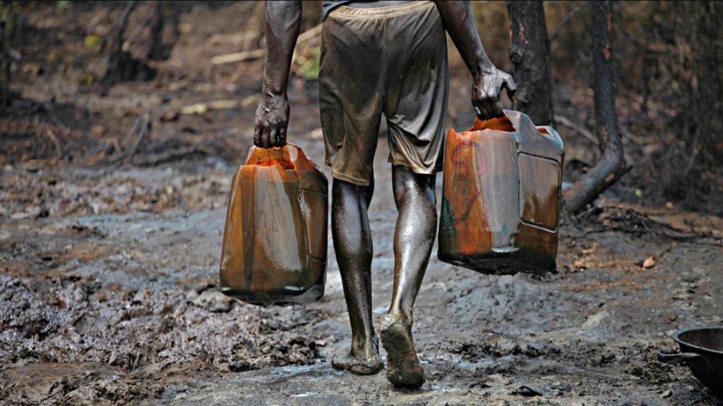 Oil pipeline leaking in a swampy area as masked men siphon crude oil; background shows rusted equipment and abandoned barrels—symbol of oil theft in Nigeria.